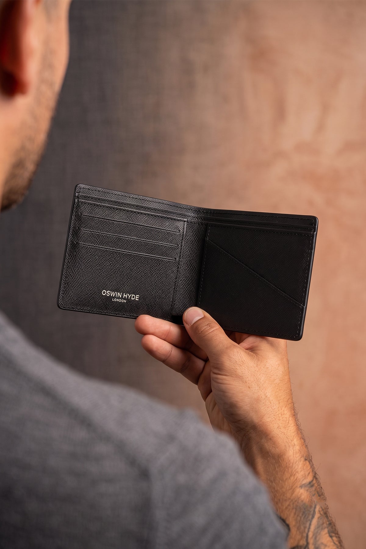 Man holding Marylebone black saffiano leather bi-fold wallet for men by Oswin Hyde – slim luxury wallet with multiple card slots and durable textured leather finish.