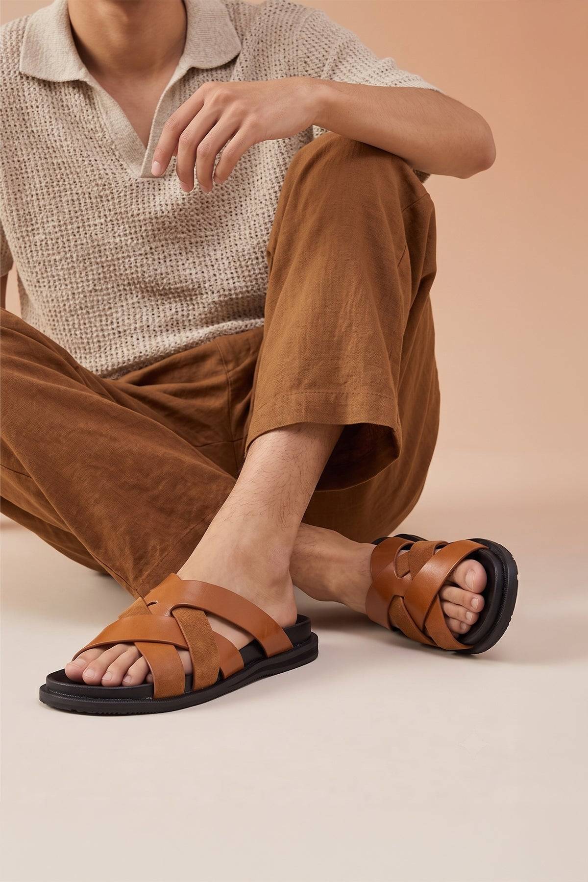 Model wearing Men’s Rowan Tan slide sandals featuring a soft suede leather X-strap design and an earthy tan finish.