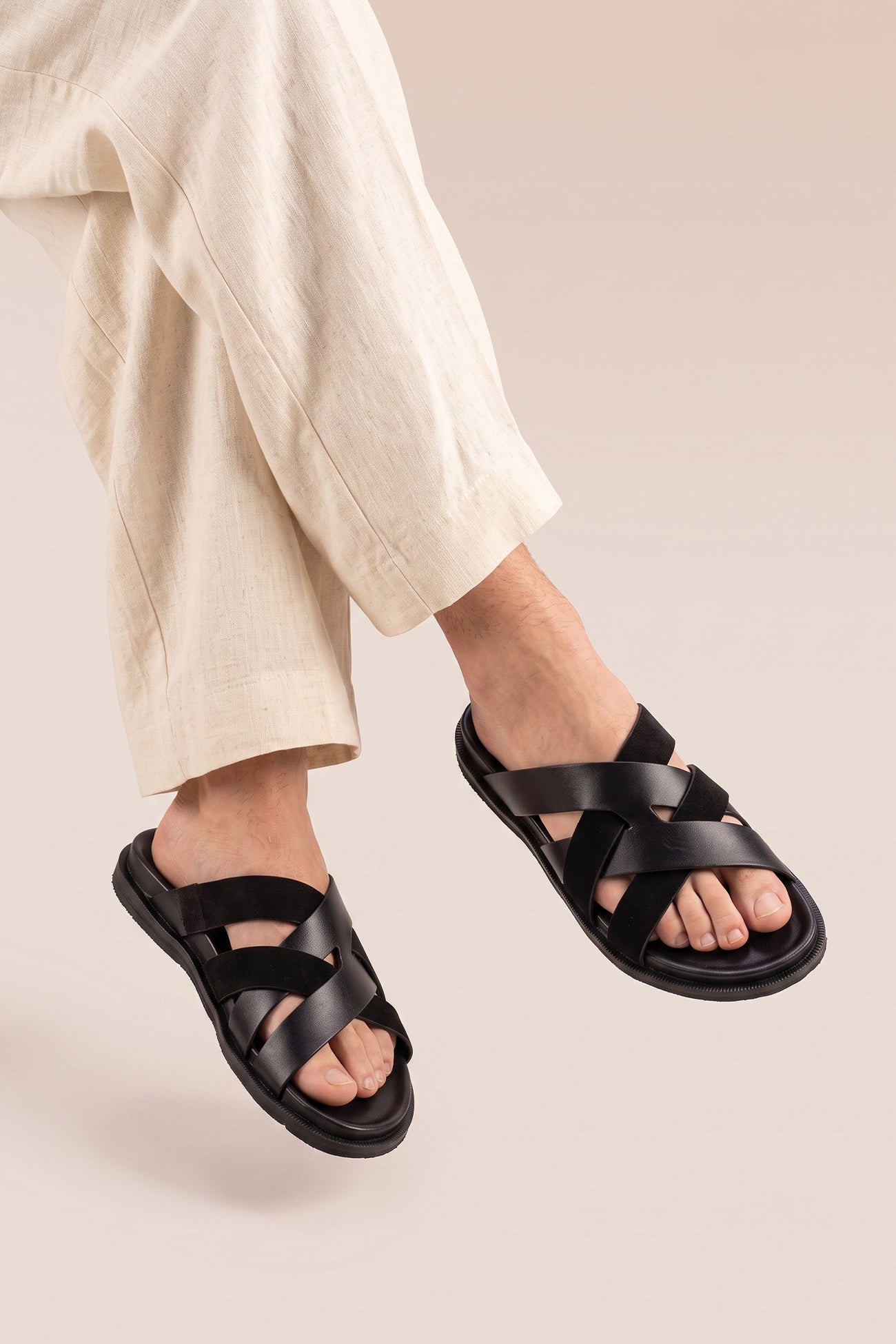 Model wearing Men’s Rowan Black slide sandals featuring a minimalist black leather X-strap design and a sleek matte finish.