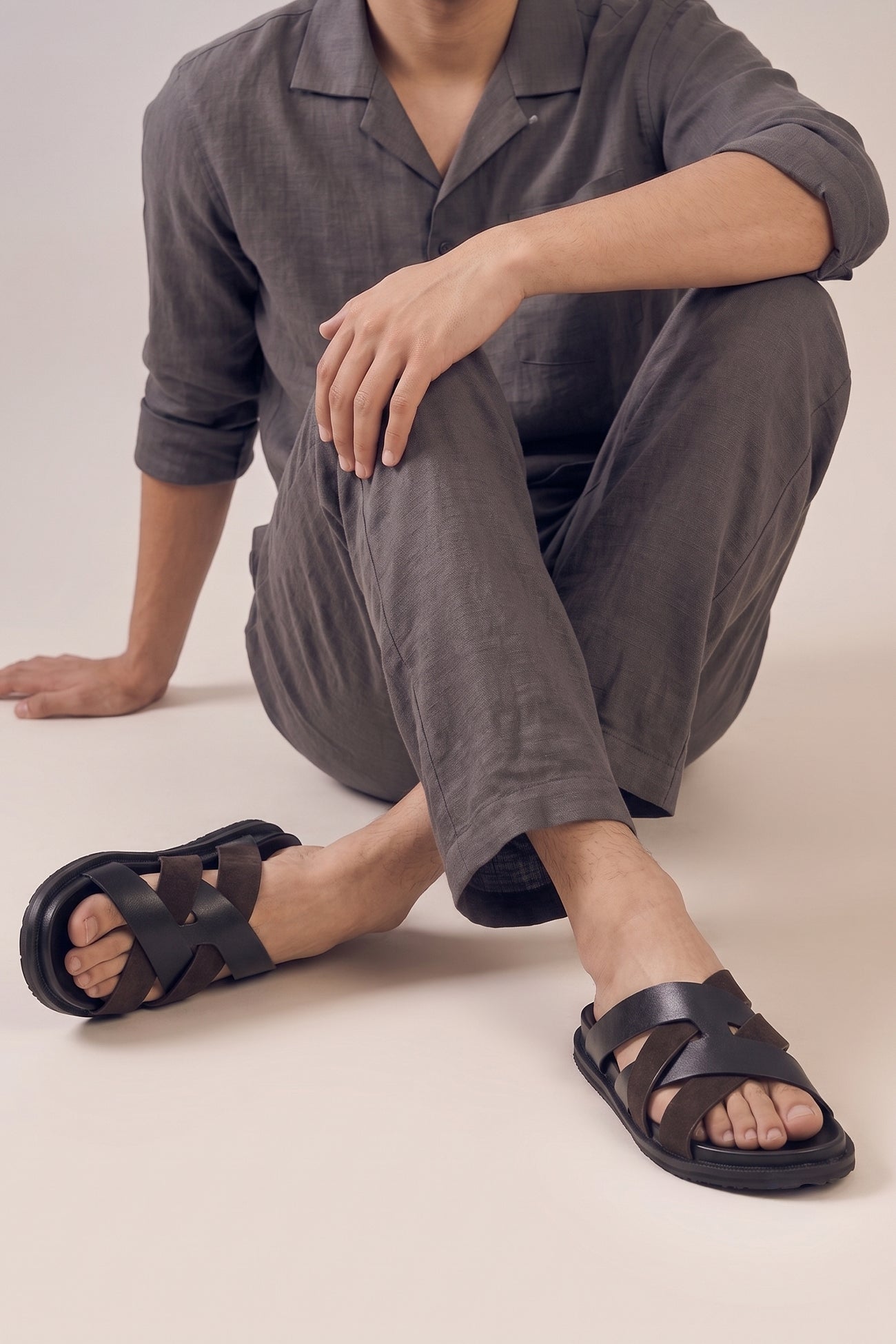 Model wearing Men’s Rowan Brown slide sandals featuring a textured brown suede X-strap design and a cushioned sole.