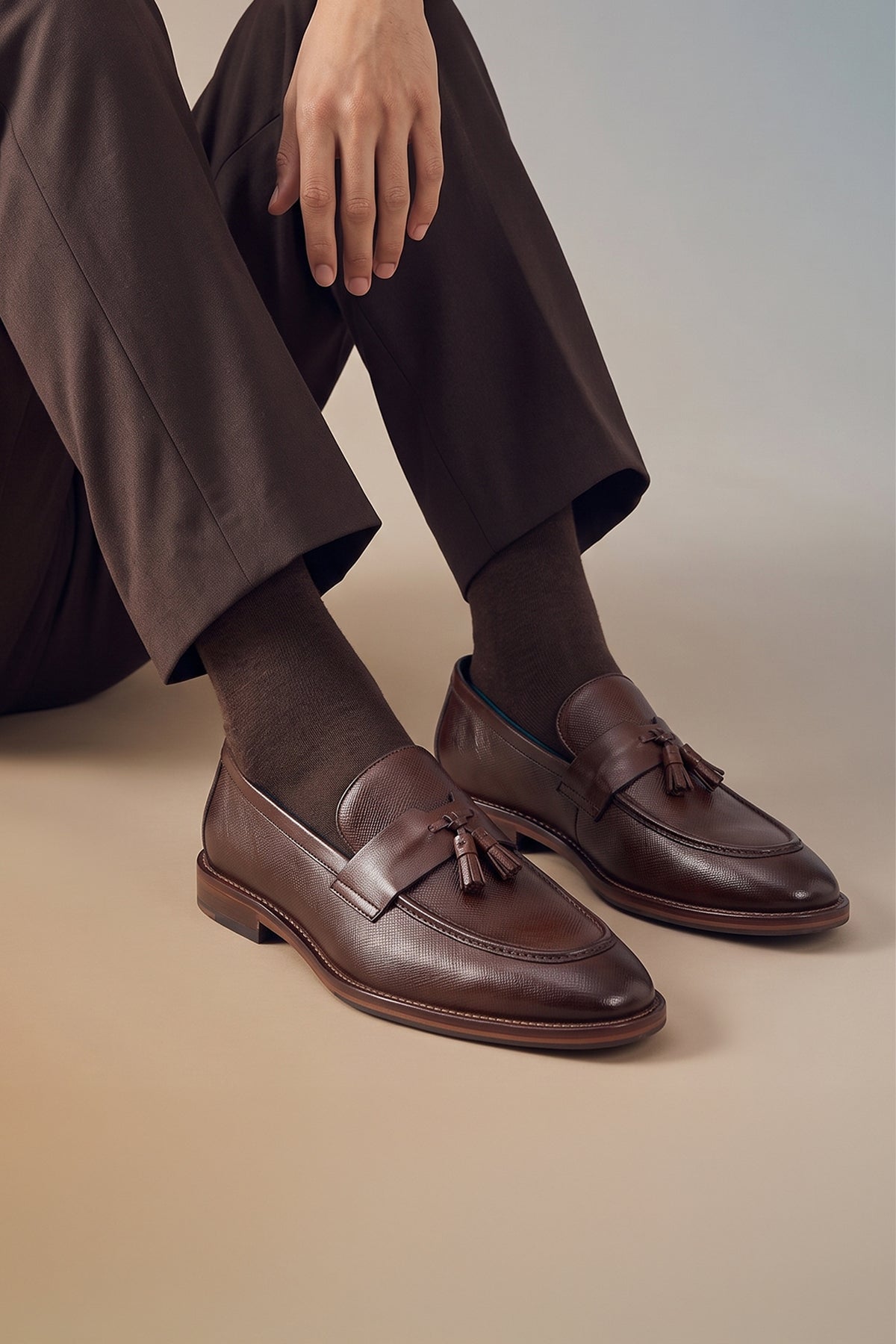 Man wearing Premium brown leather tassel loafers for men featuring a textured finish, burnished moc-toe details, decorative leather tassels, and a cushioned teal interior.