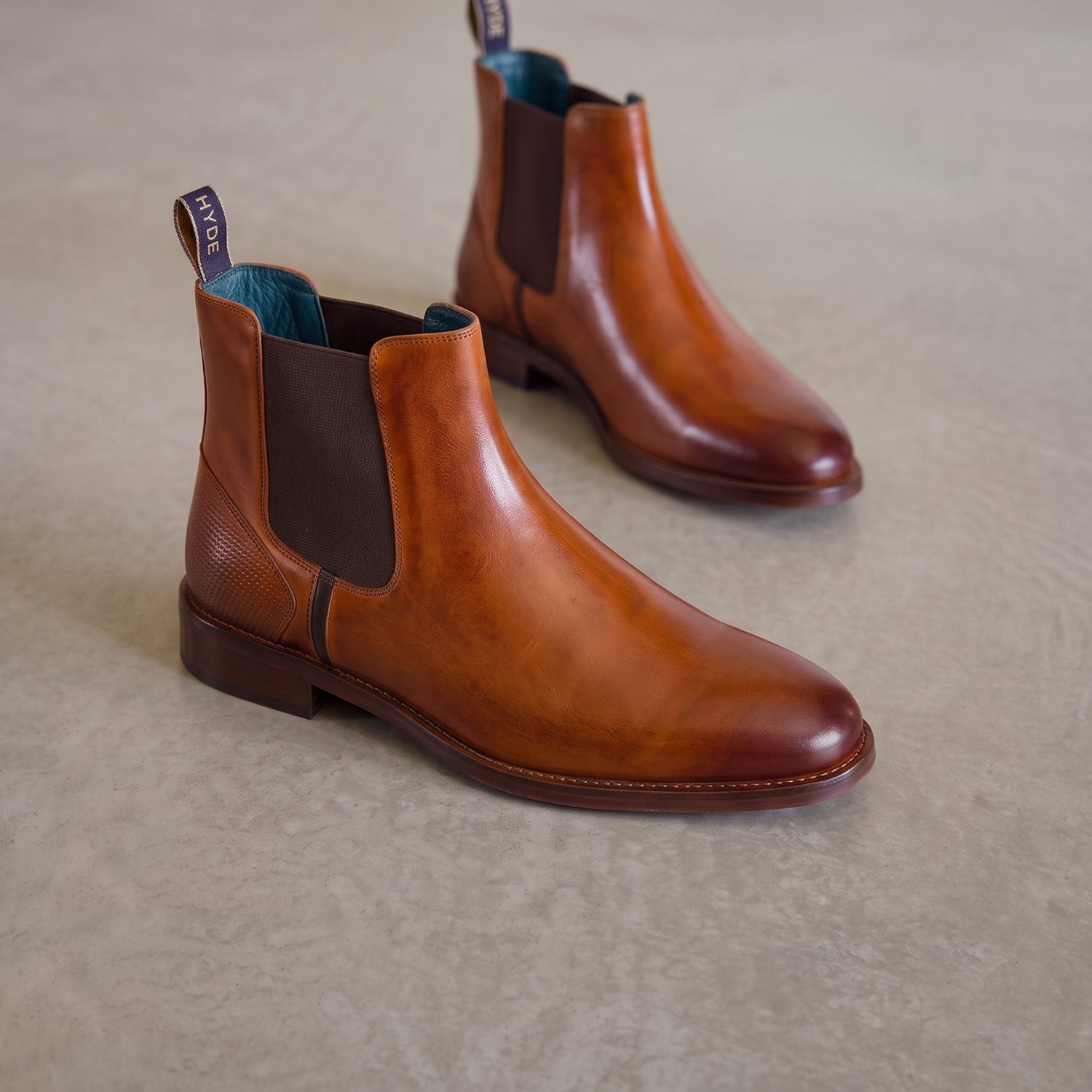Premium men's tan leather Chelsea boots by Oswin Hyde, showcasing a polished cognac finish, brown elasticated side gussets, branded heel loops, and a signature teal interior lining.