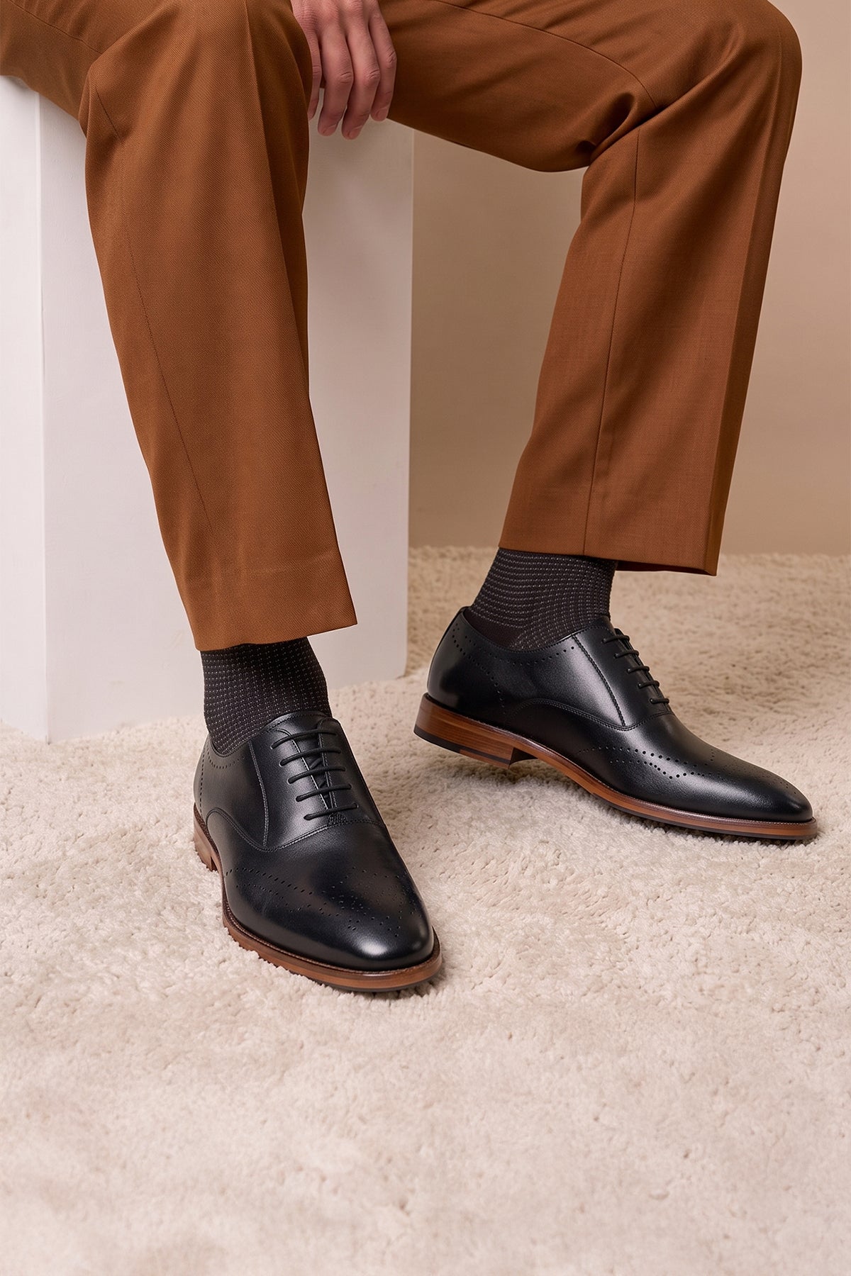 Man wearing Oswin Hyde London premium black leather wingtip brogues with a toe medallion pattern, contrast welt stitching, and a cushioned teal interior.