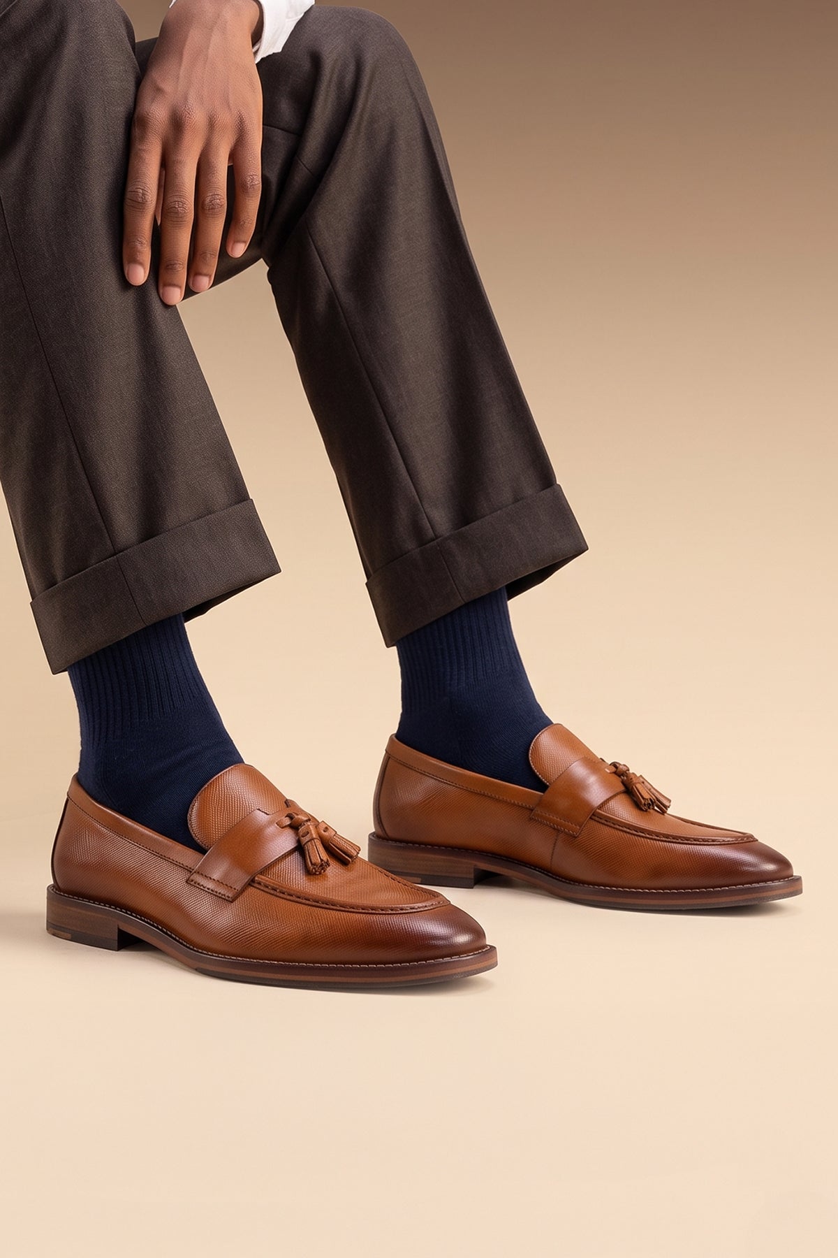 Model wearing Premium tan leather tassel loafers for men featuring a textured finish, burnished moc-toe details, decorative leather tassels, and a cushioned teal interior.