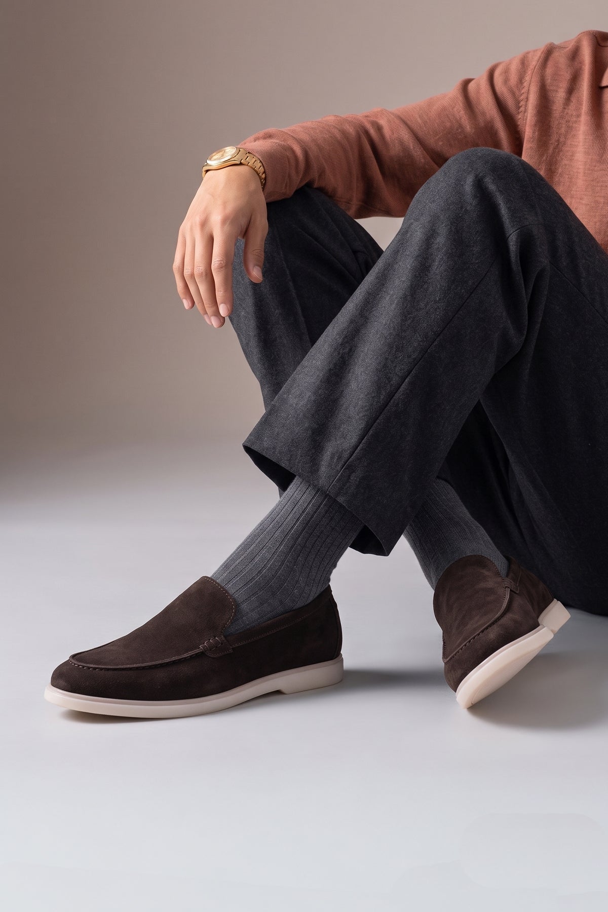 A person wearing Oswin Hyde Morgan brown suede loafers with charcoal grey trousers and ribbed grey socks.