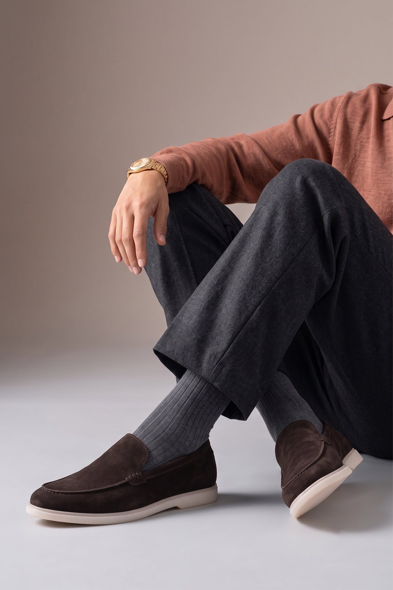 A person wearing Oswin Hyde Morgan brown suede loafers with charcoal grey trousers and ribbed grey socks.