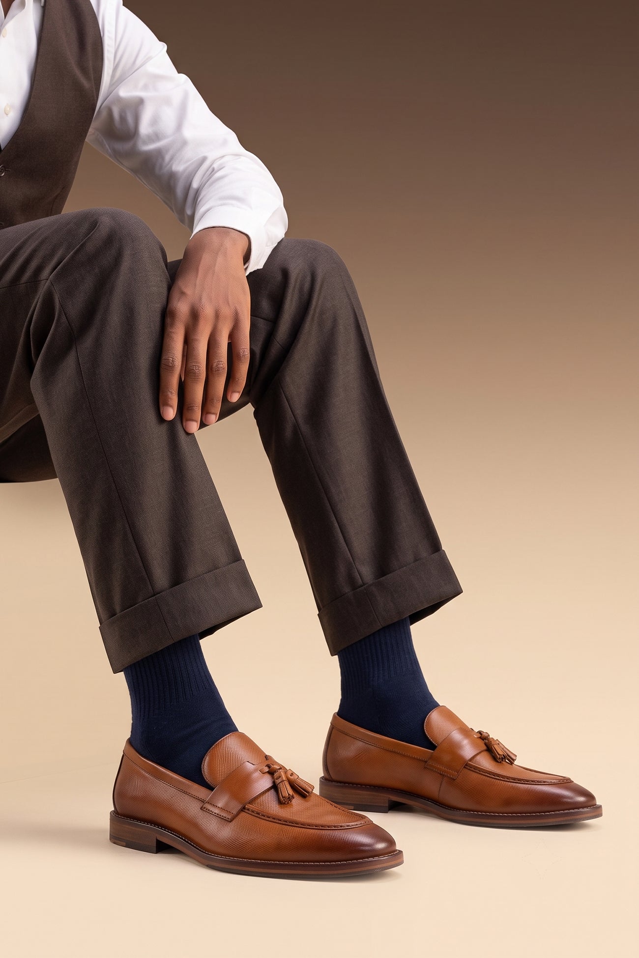 Man wearing Premium tan leather tassel loafers for men featuring a textured finish, burnished moc-toe details, decorative leather tassels, and a cushioned teal interior.