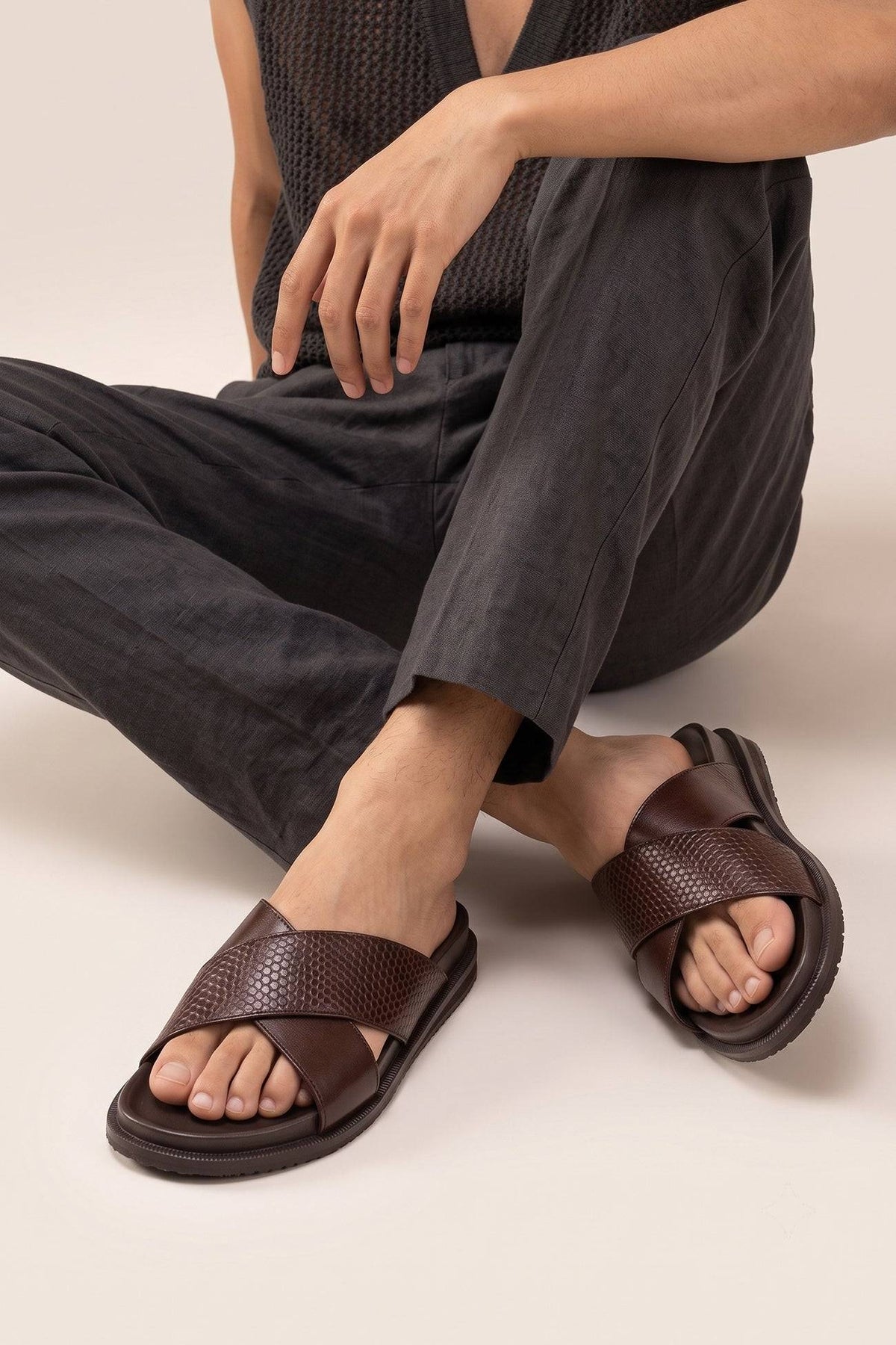 Nyle Brown cross strap sandals for men by Oswin Hyde with stylish design and comfortable fit worn on a wooden floor by a sitting model