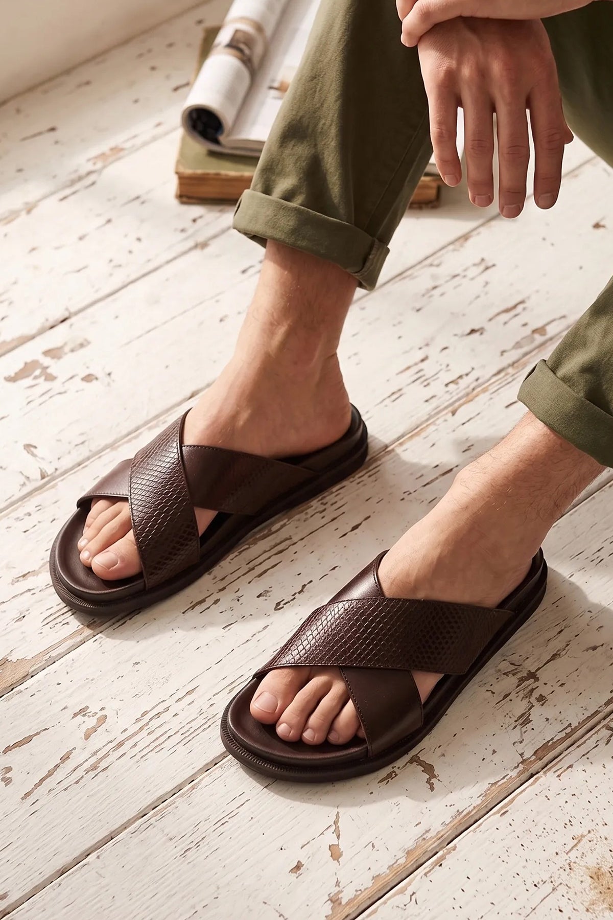 Nyle Brown cross strap sandals for men by Oswin Hyde with stylish design and comfortable fit worn on a wooden floor by a sitting model