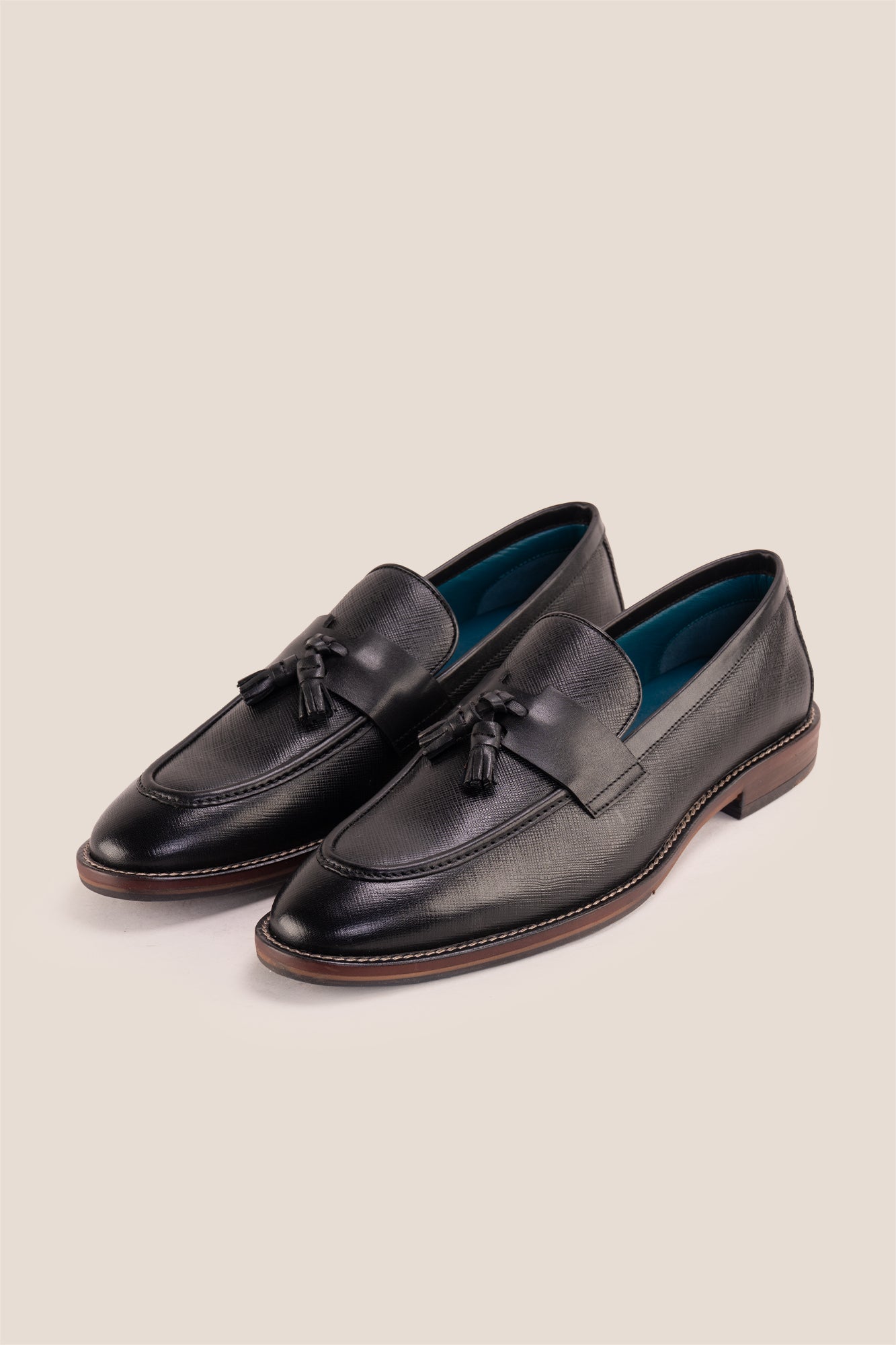 Premium black leather tassel loafers for men featuring a textured finish, burnished moc-toe details, decorative leather tassels, and a cushioned teal interior.