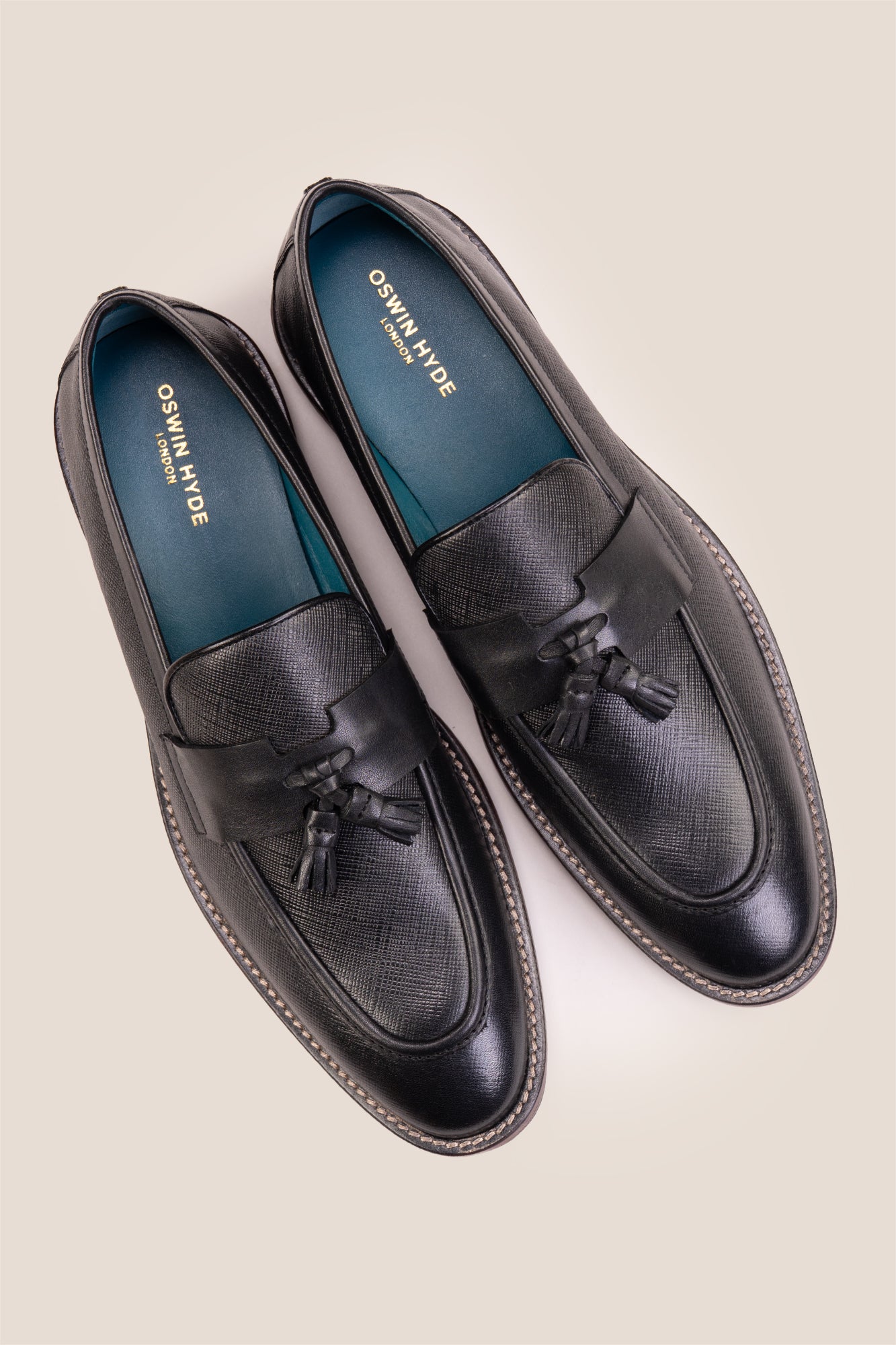 Premium black leather tassel loafers for men featuring a textured finish, burnished moc-toe details, decorative leather tassels, and a cushioned teal interior.