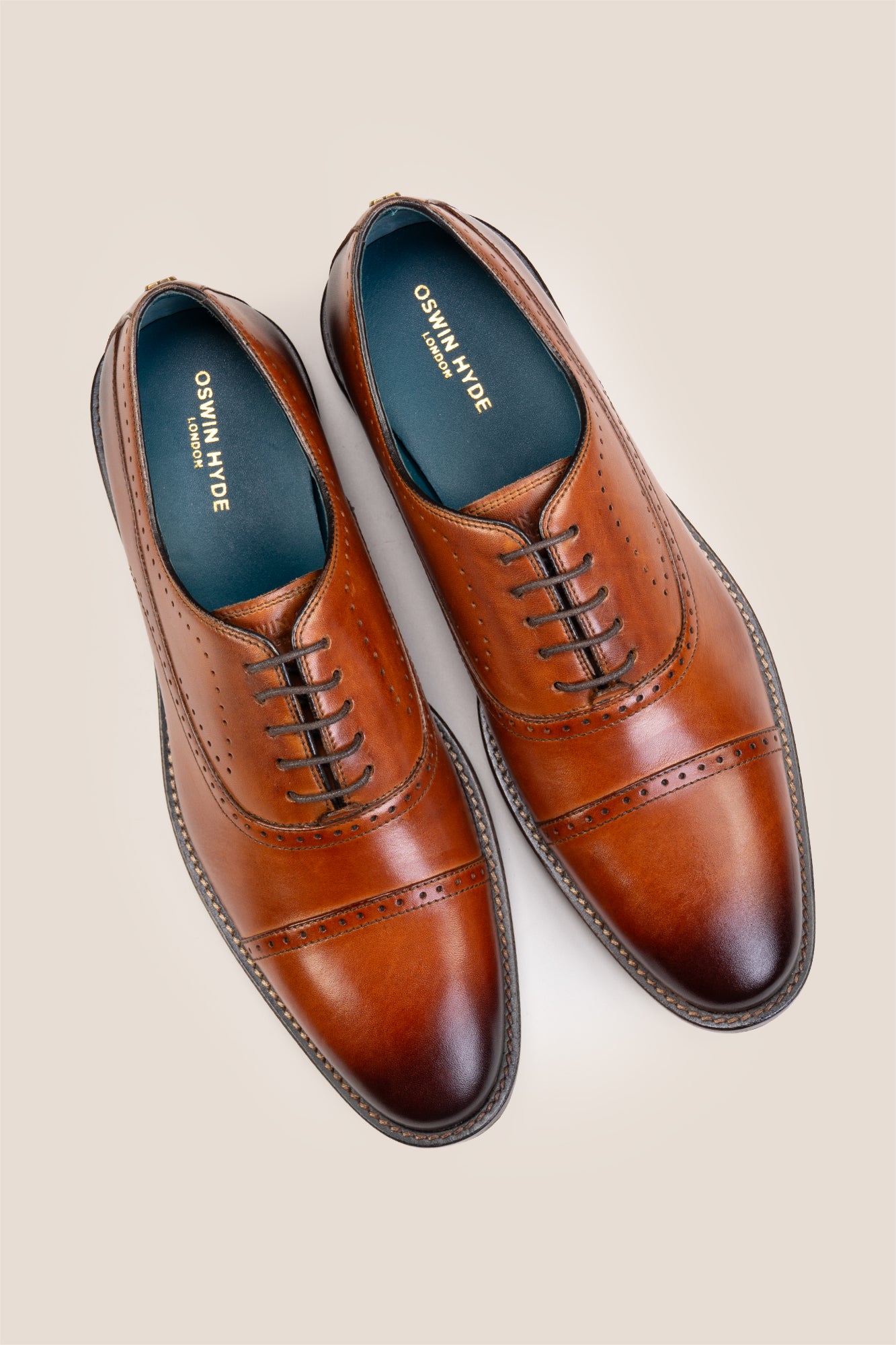 Premium men's tan leather oxford shoes by Oswin Hyde London, featuring a cap toe with decorative perforations, closed lacing, contrast welt stitching, and a cushioned teal interior.