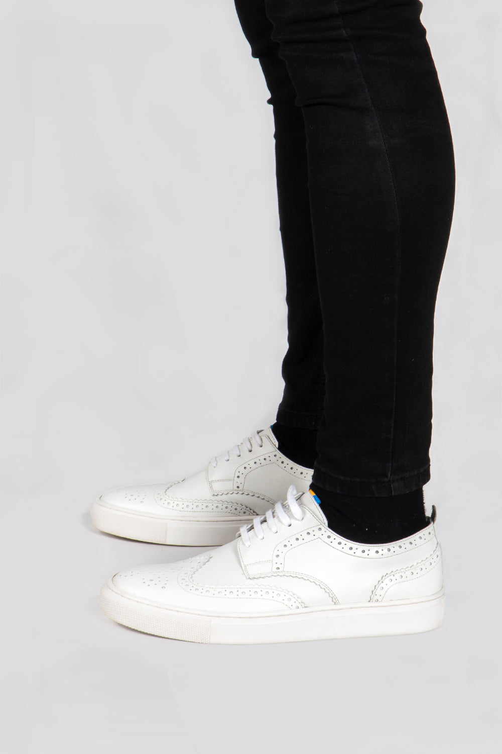 White leather men’s wingtip brogue trainers with perforated detailing, cushioned sole and a refined silhouette—ideal for stylish smart-casual wear.