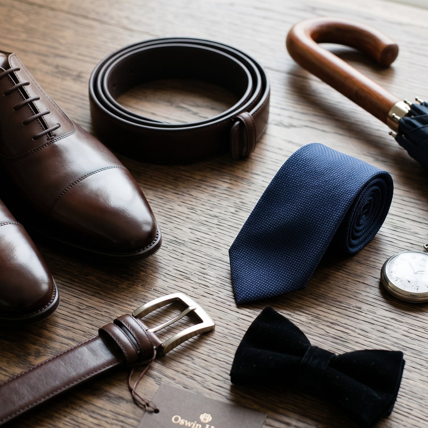 Leather shoes with leather belt, silk tie, bow tie and an umbrella on a table