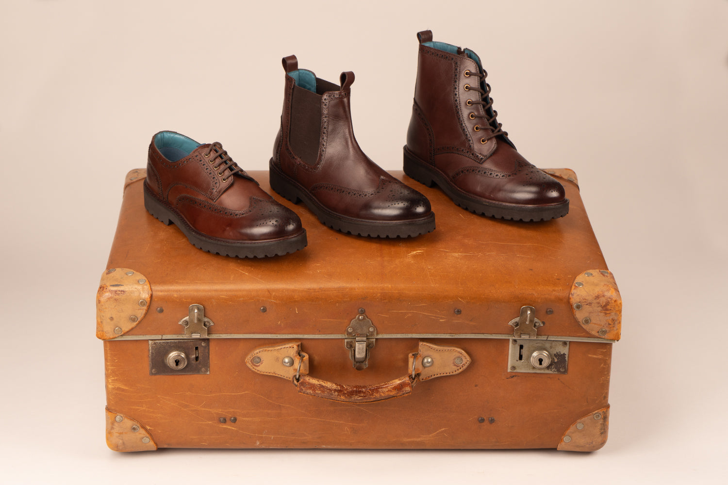 brogue shoe, brogue boot and a cheseal boot on top of a leather suitcase. 