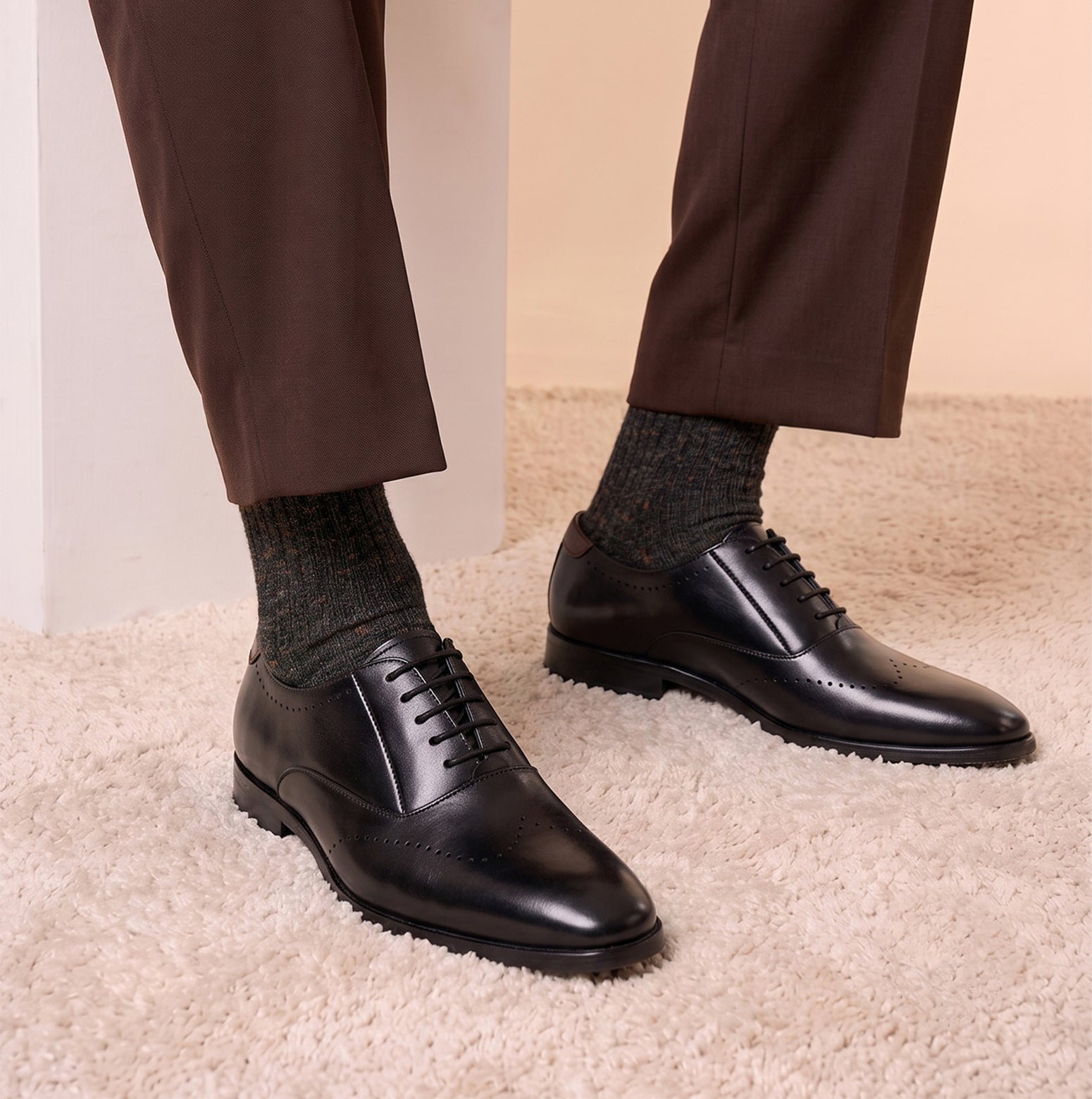 Man wearing Oswin Hyde London premium black leather wingtip brogues with a toe medallion pattern, contrast welt stitching, and a cushioned teal interior.
