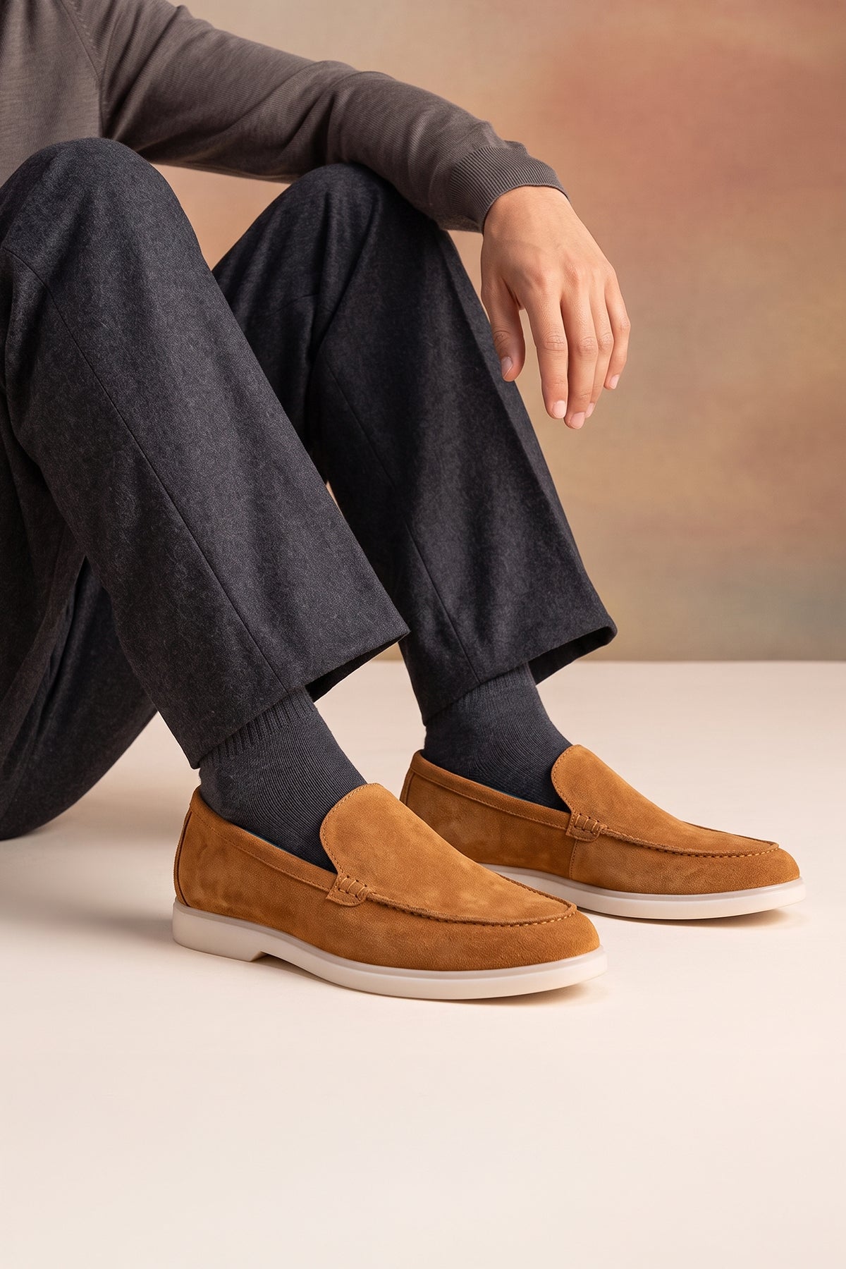 A person wearing Oswin Hyde Morgan brown suede loafers with charcoal grey trousers and ribbed grey socks.