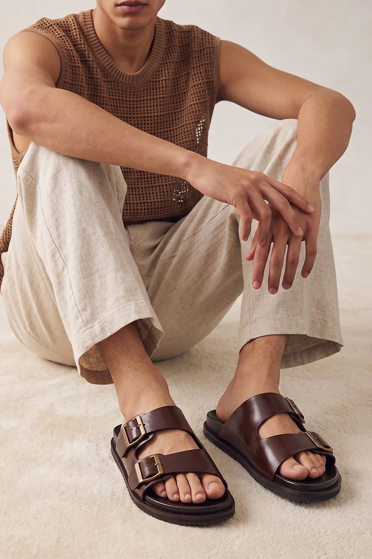 Model wearing Jude Brown leather men's sandals with broad twin buckle straps and a contoured footbed, designed for comfort and summer style.