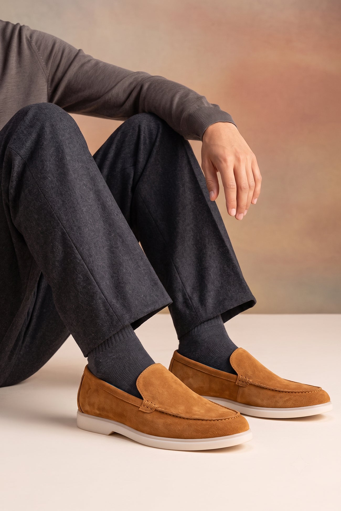 A person wearing Oswin Hyde Morgan brown suede loafers with charcoal grey trousers and ribbed grey socks.