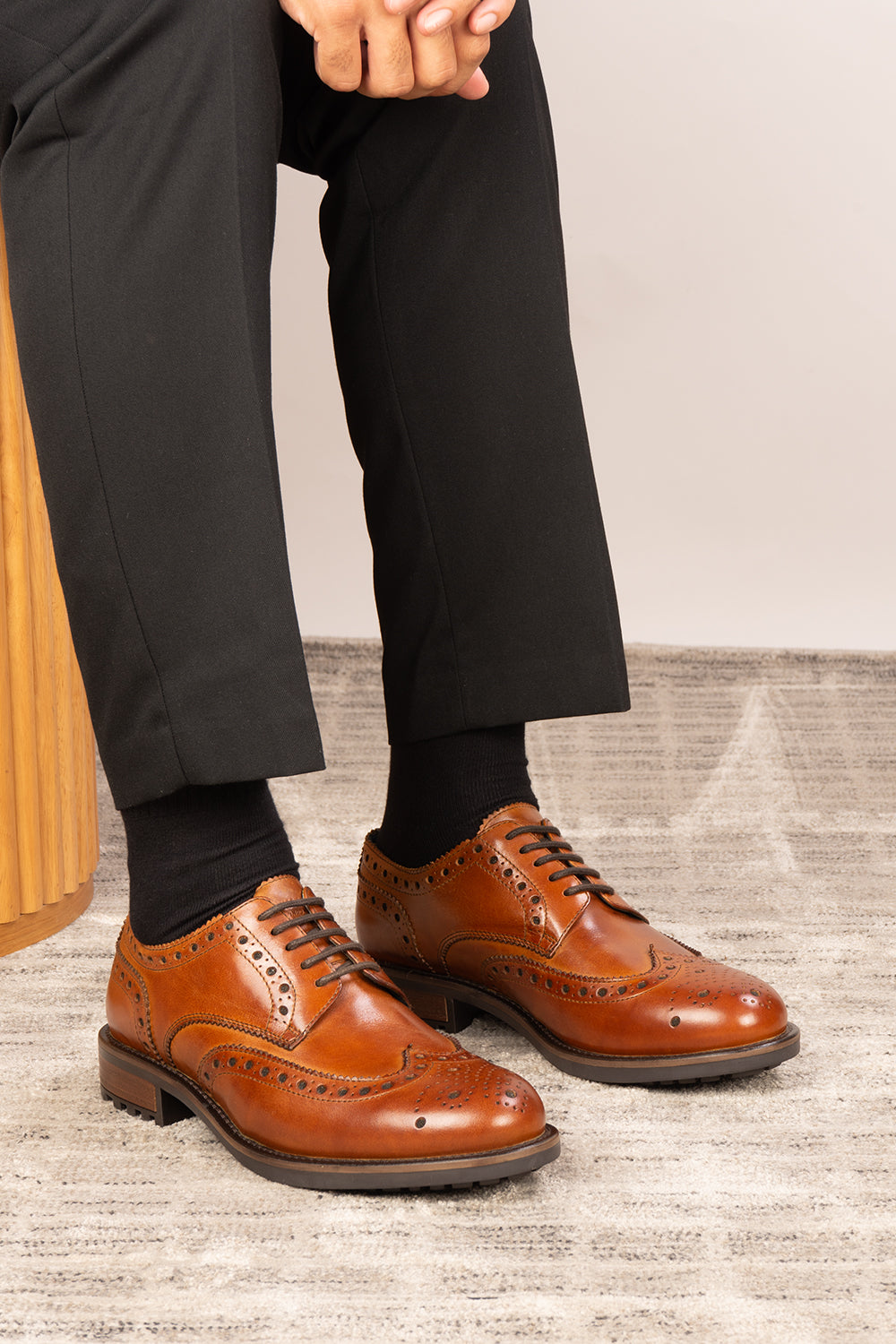 Brown dress shoes worn with black pants and socks on a neutral background