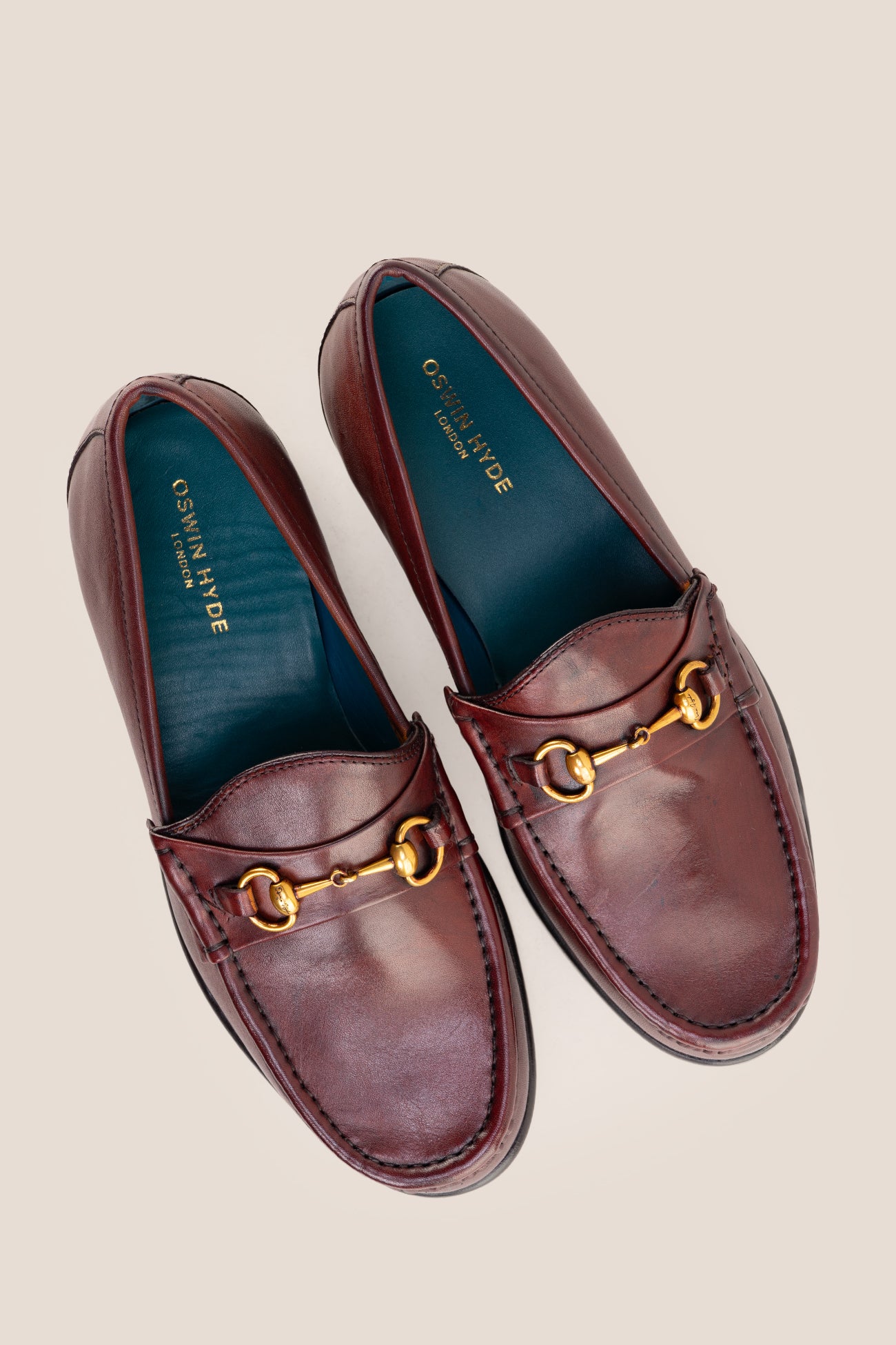 Pair of Oswin Hyde Samuel Bordo burgundy leather horsebit loafers with gold buckle detail and teal lining.