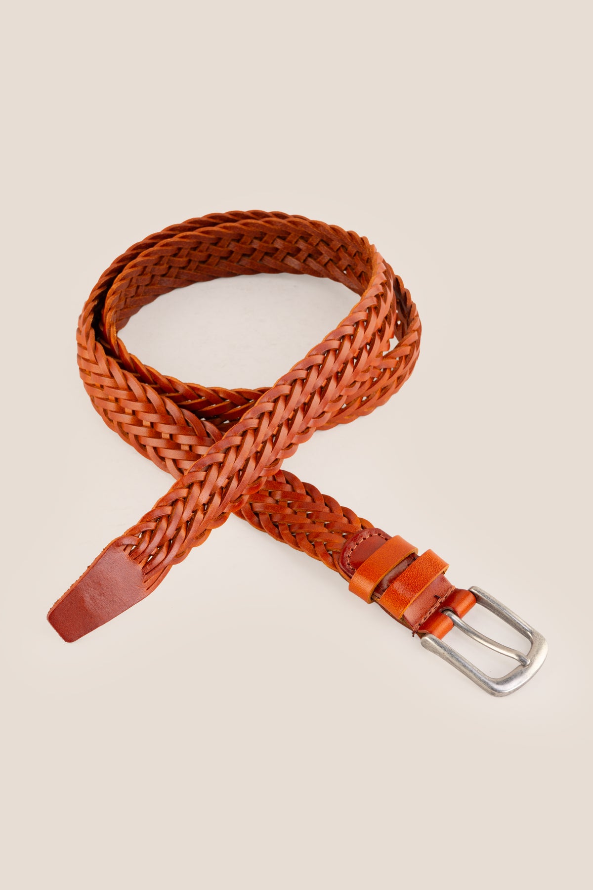 Milo tan braided leather belt styled in a crossed loop arrangement against a beige background.