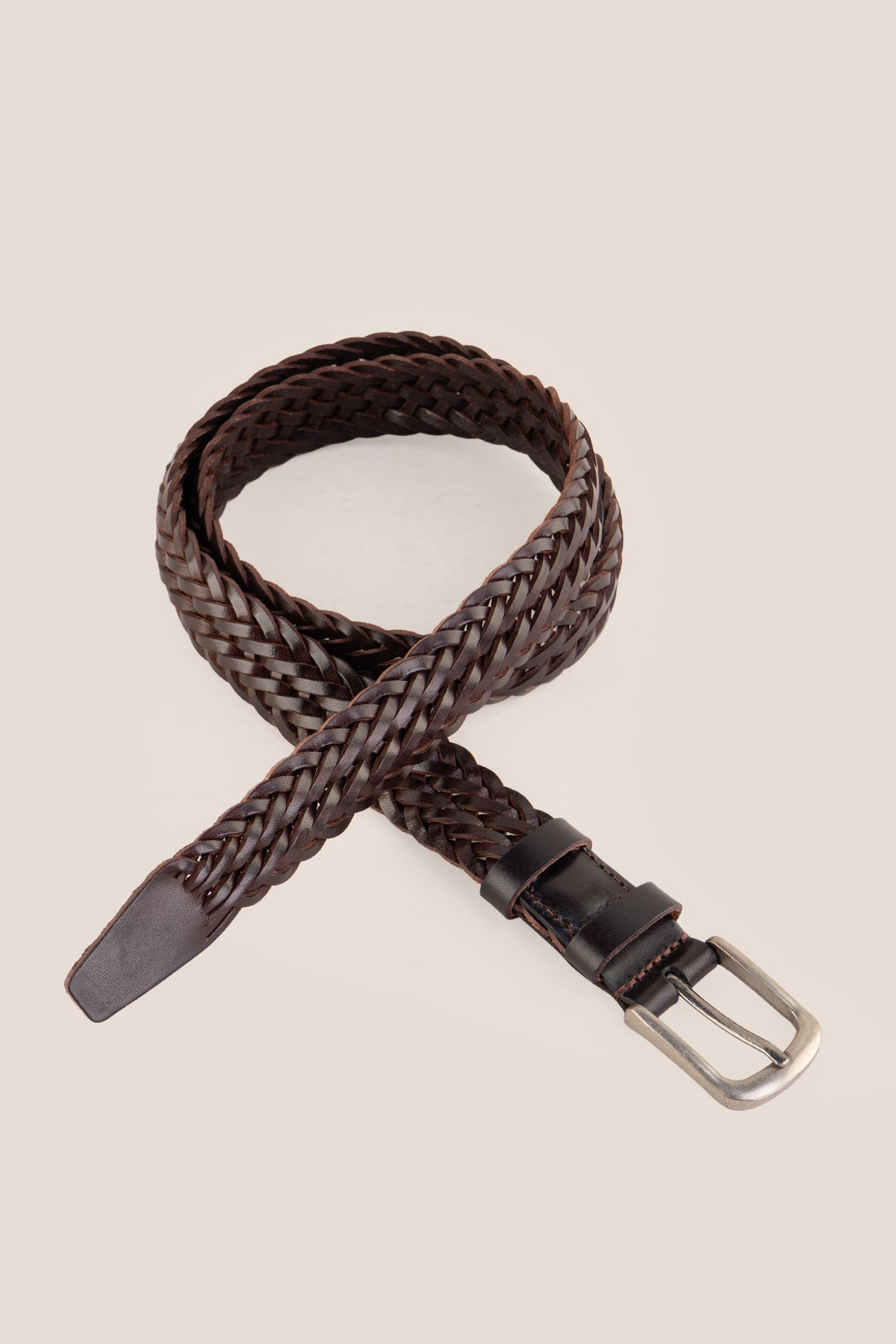 Milo brown braided leather belt arranged in a crossed loop pattern against a beige background.