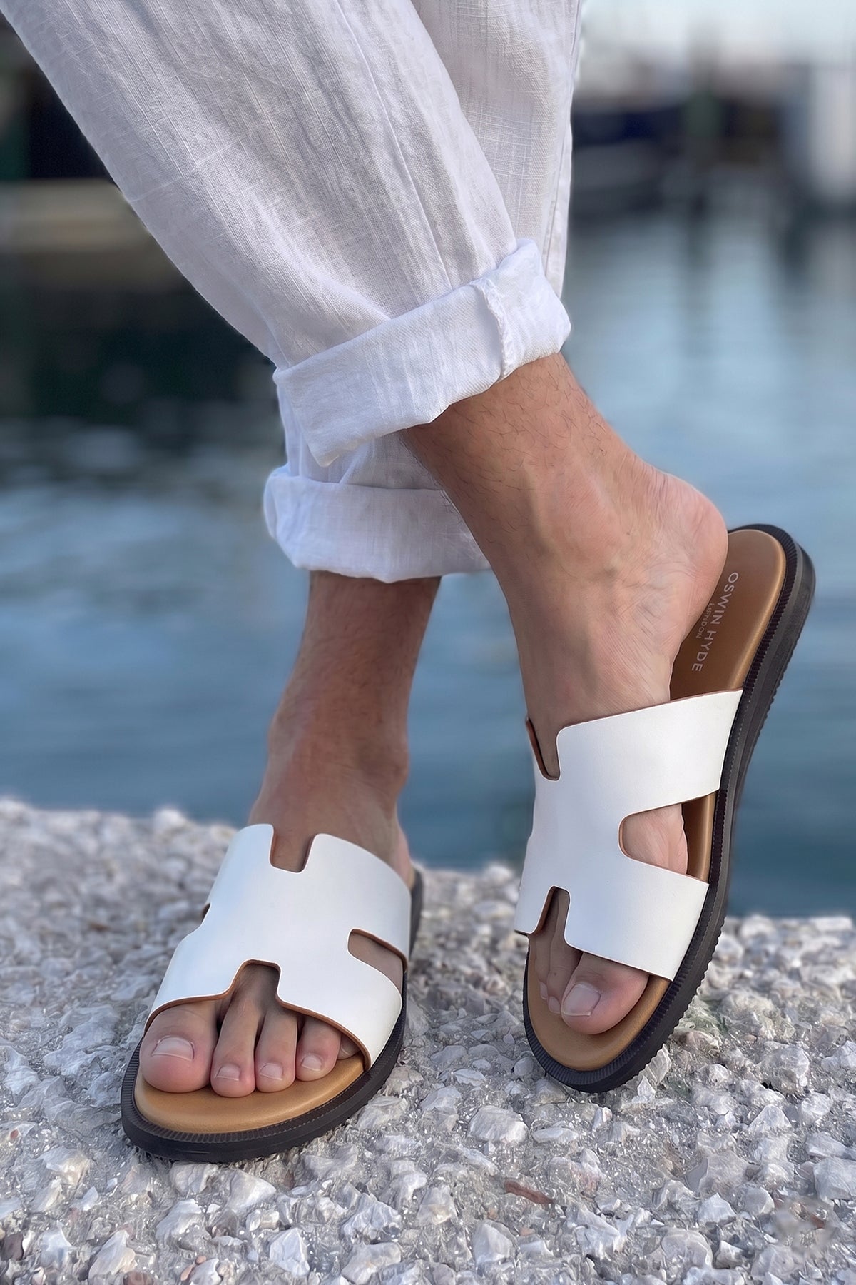 Model wearing Men’s Phoenix White sandals in premium white leather featuring a minimalist hyde strap H-frame design.