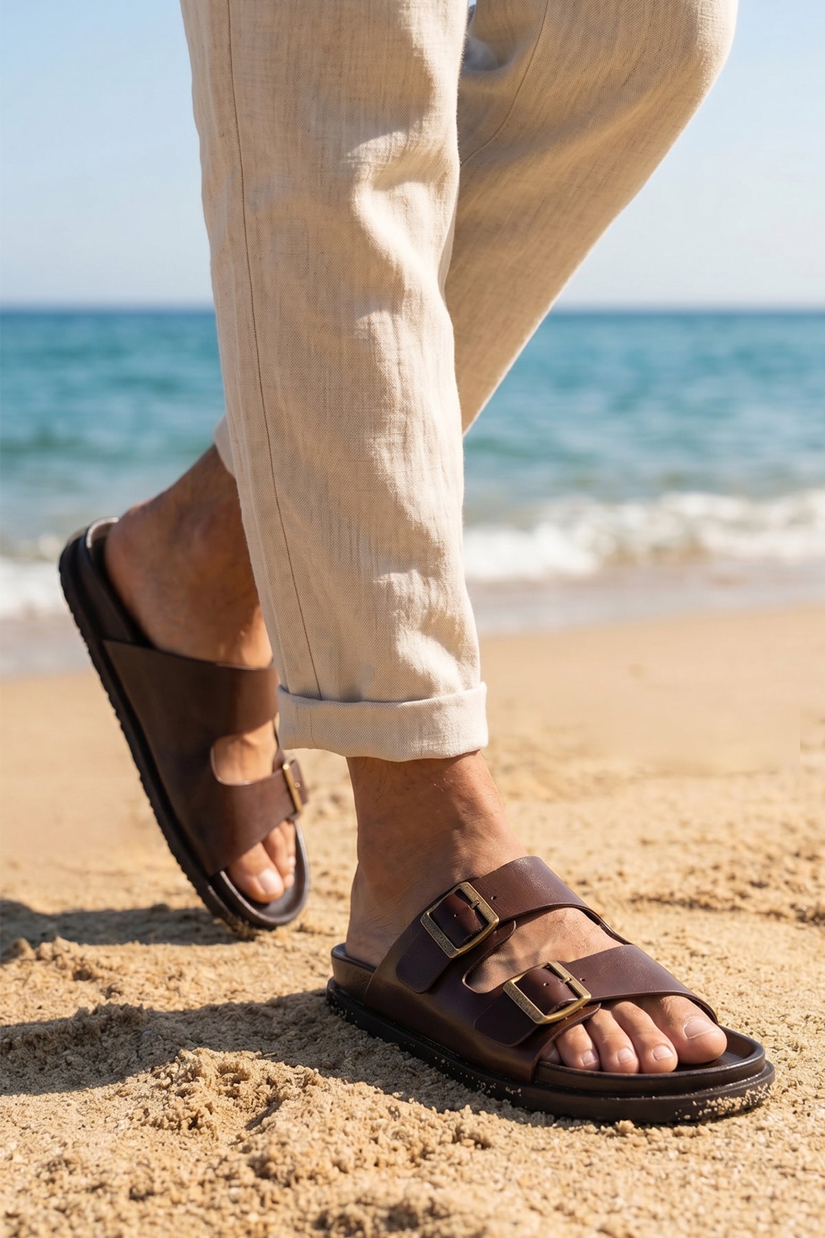 Mode wearing Jude Brown leather men's sandals with broad twin buckle straps and a contoured footbed, designed for comfort and summer style.