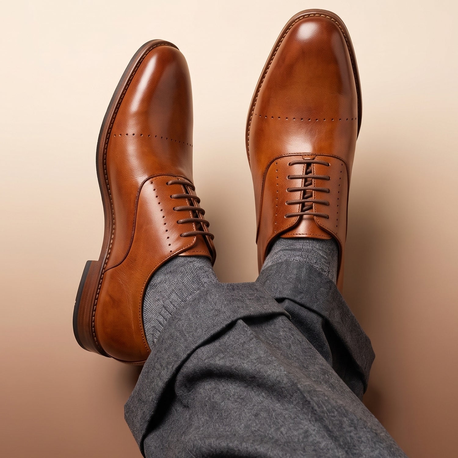 Classic men's business workwear featuring tan leather oxford shoes with subtle perforation detailing across the cap toe, styled with grey dress trousers and matching laces.