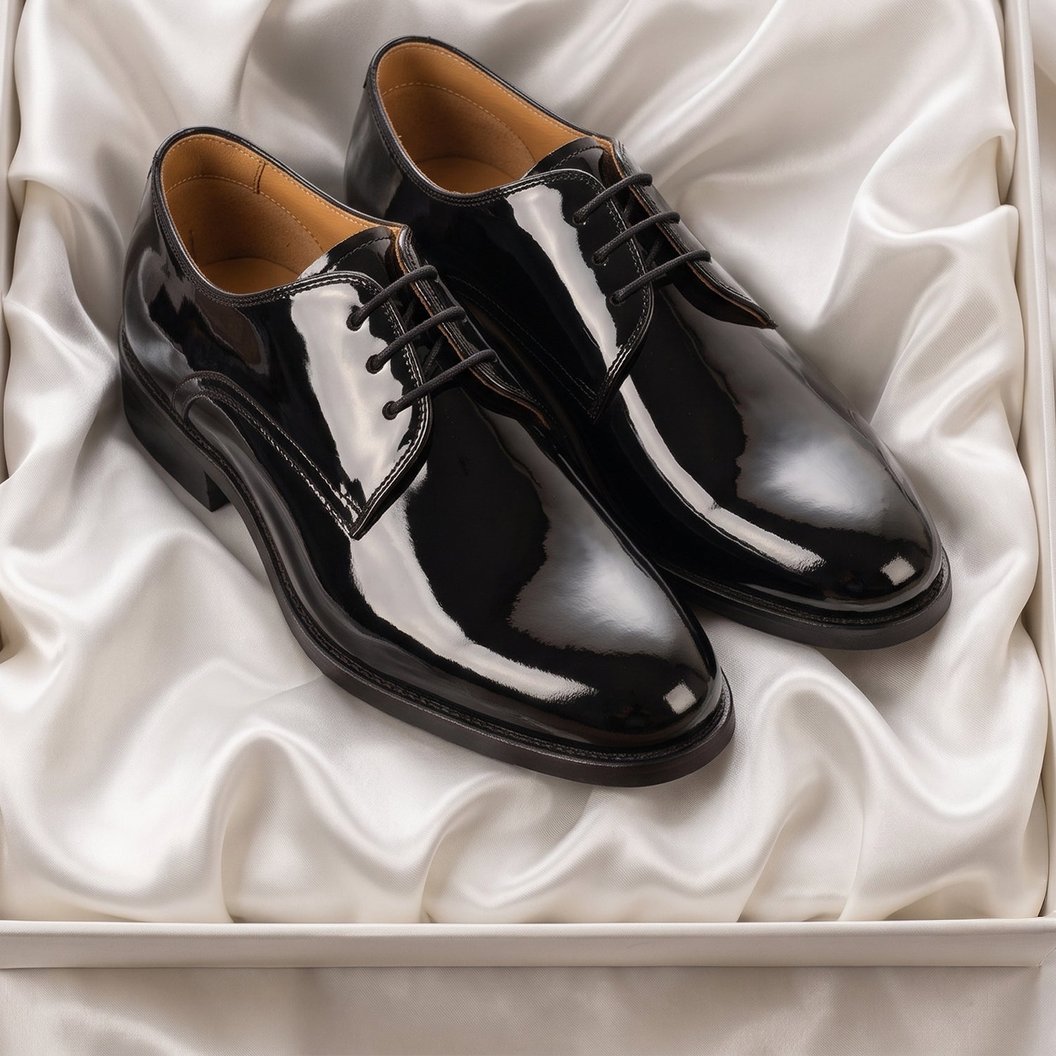 Premium men's black patent leather tuxedo shoes, ideal for formal wedding guest attire, displayed on elegant white silk lining with a tan leather interior.