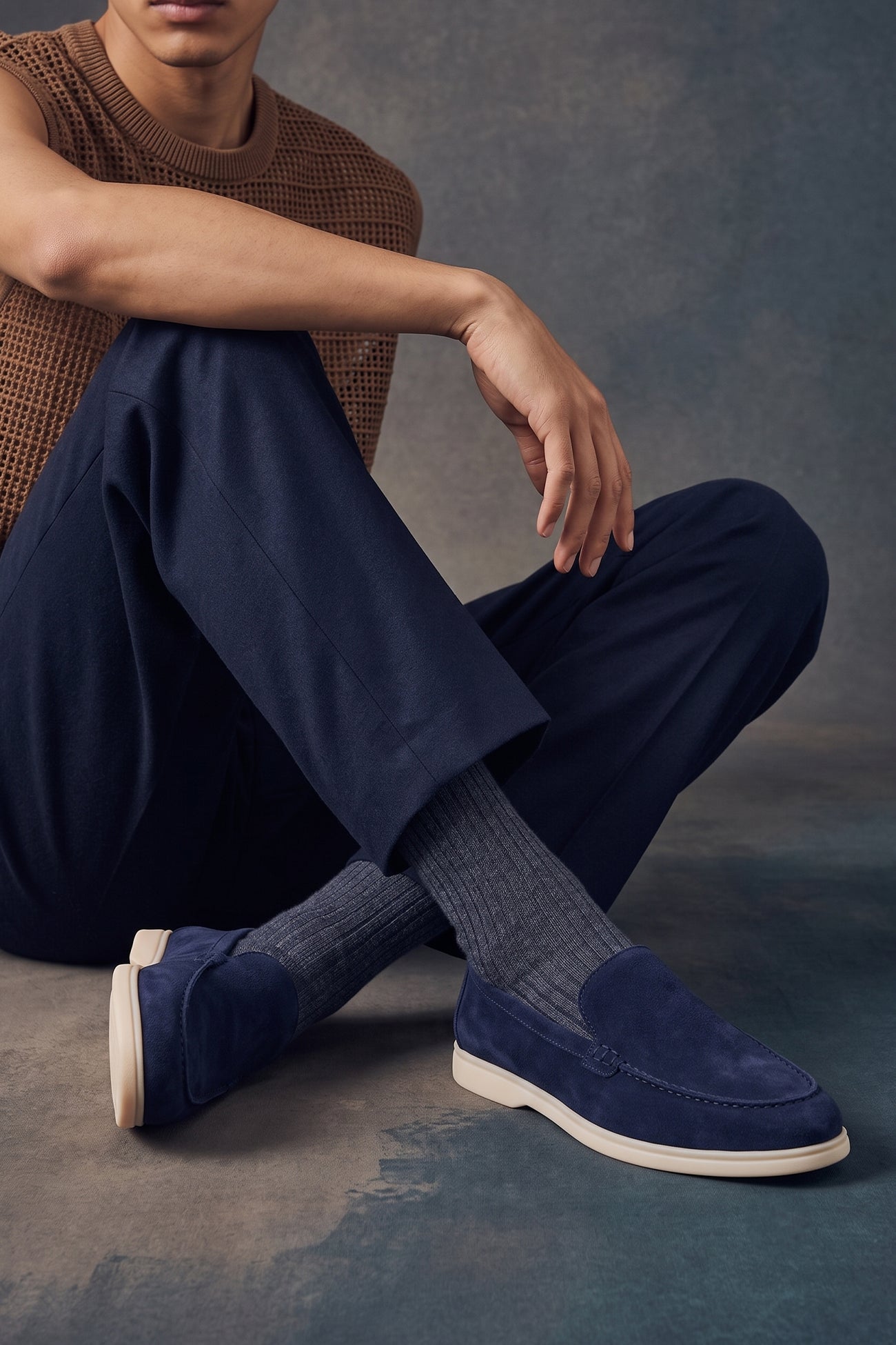 A person wearing Oswin Hyde Morgan Navy suede loafers with navy trousers and ribbed grey socks.