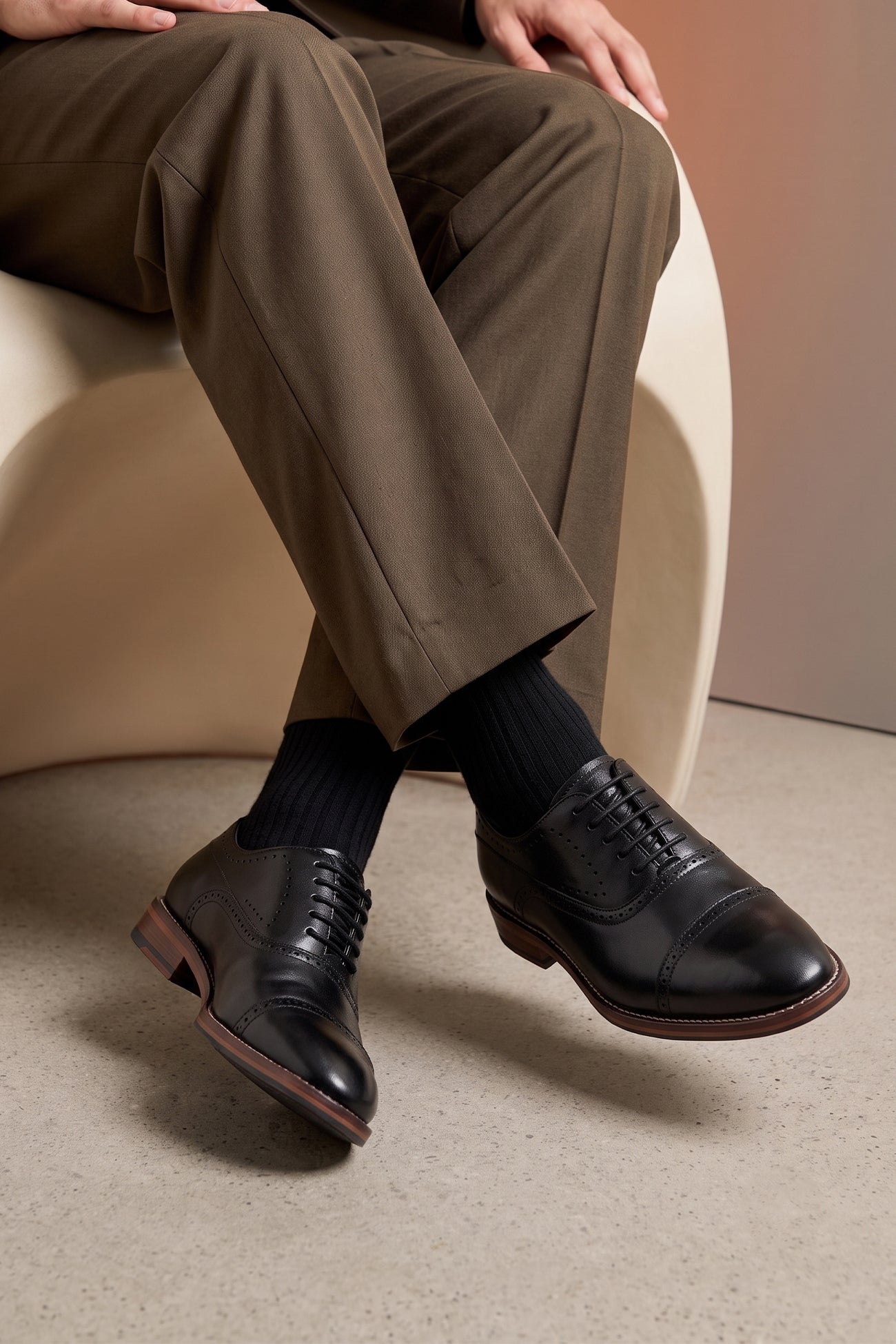 Man wearing Premium men's black leather oxford shoes by Oswin Hyde London, featuring a cap toe with decorative perforations, closed lacing, contrast welt stitching, and a cushioned teal interior.