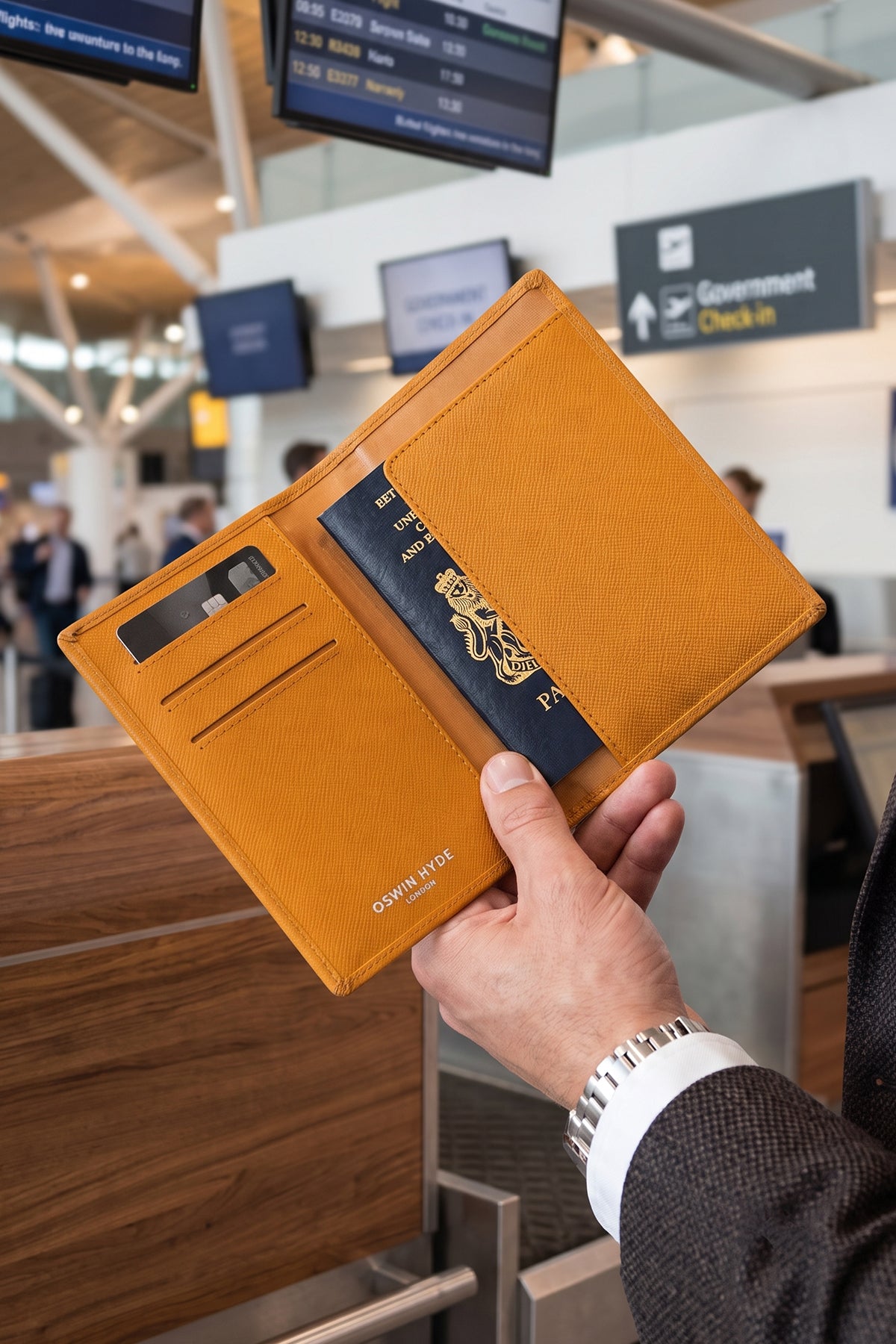 Man holding Tan saffiano leather men’s passport holder by Oswin Hyde – slim and stylish travel accessory with secure slot and textured finish.