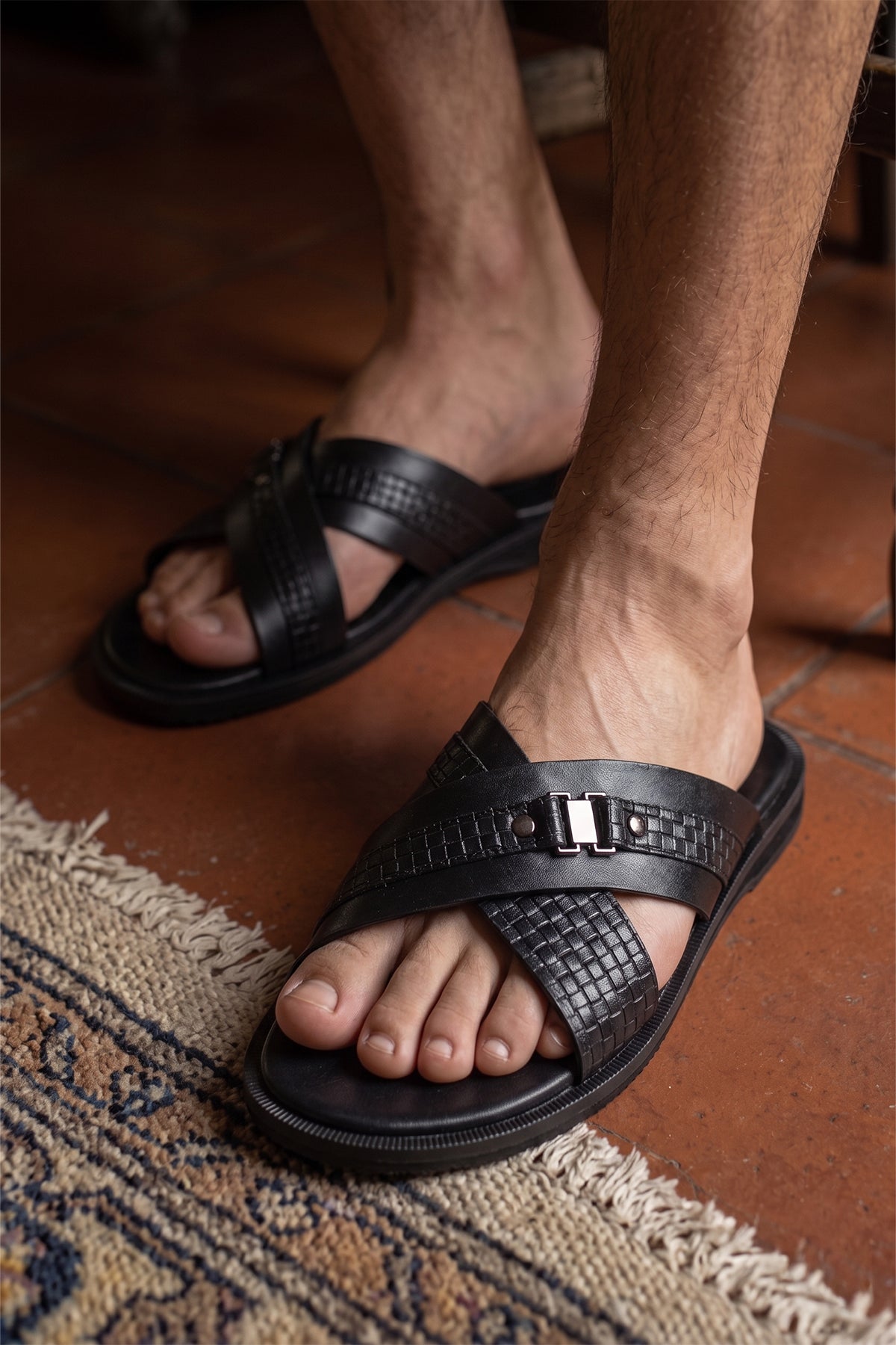 Aiden Black men’s leather sandals with a unique woven criss-cross strap design indoors.
