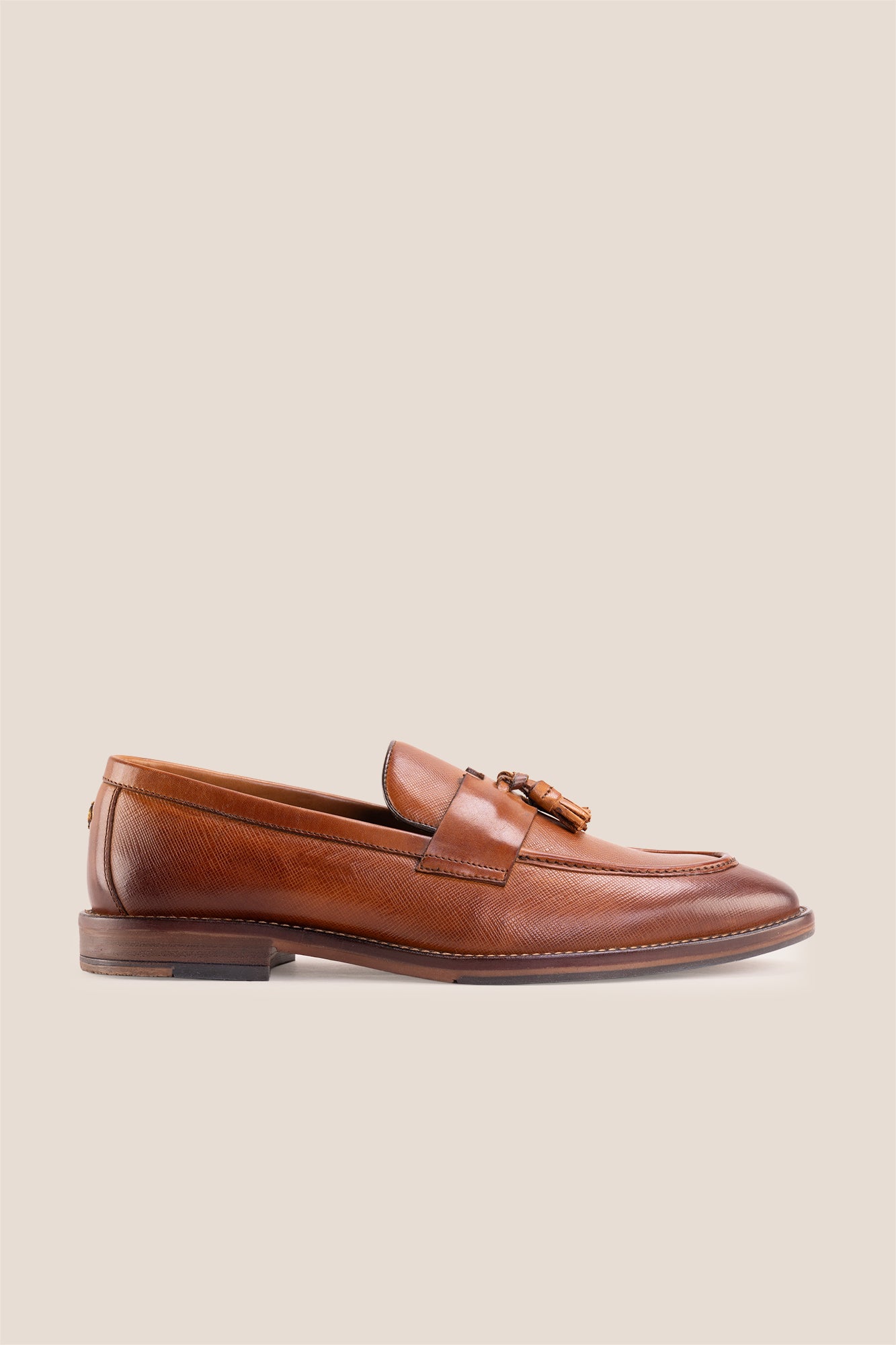 Premium tan leather tassel loafers for men featuring a textured finish, burnished moc-toe details, decorative leather tassels, and a cushioned teal interior.