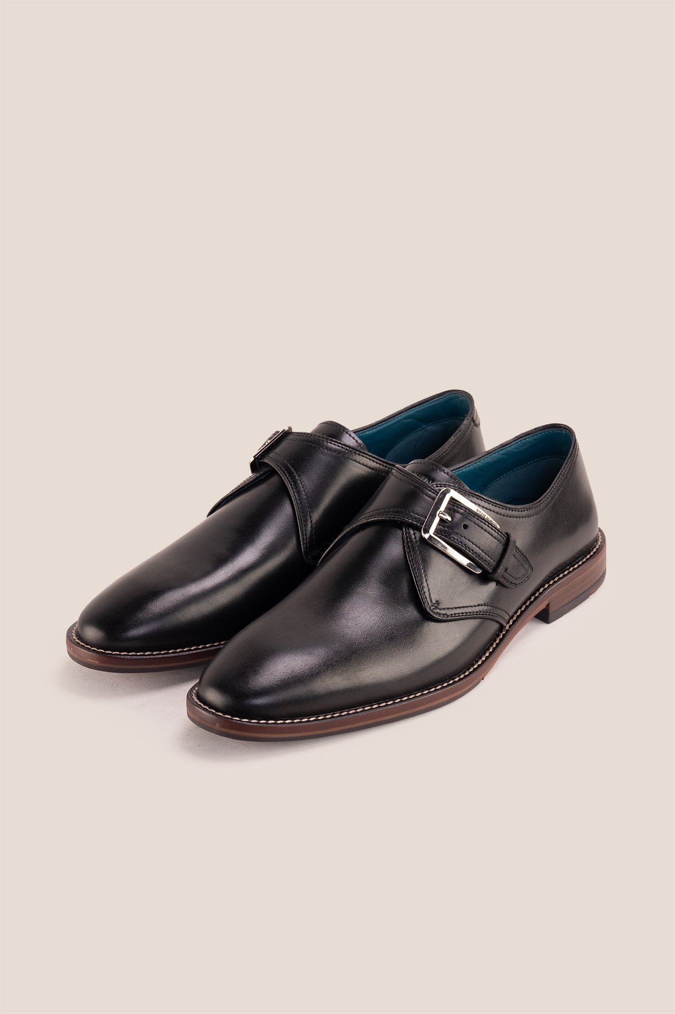 Premium men's black leather single monk strap dress shoes by Oswin Hyde London featuring a plain toe, adjustable silver buckle, contrast sole stitching, and a cushioned teal interior.