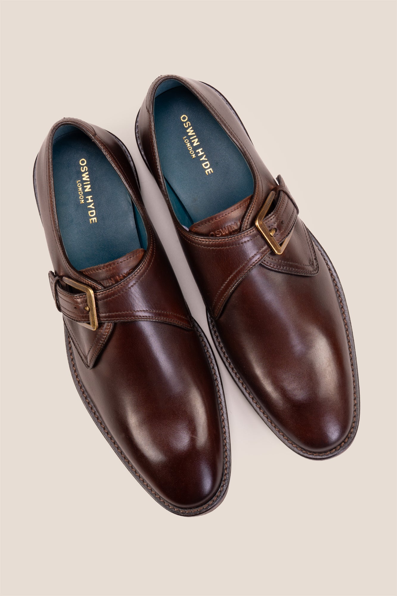 Premium men's brown leather single monk strap dress shoes by Oswin Hyde London featuring a plain toe, adjustable golden buckle, contrast sole stitching, and a cushioned teal interior.