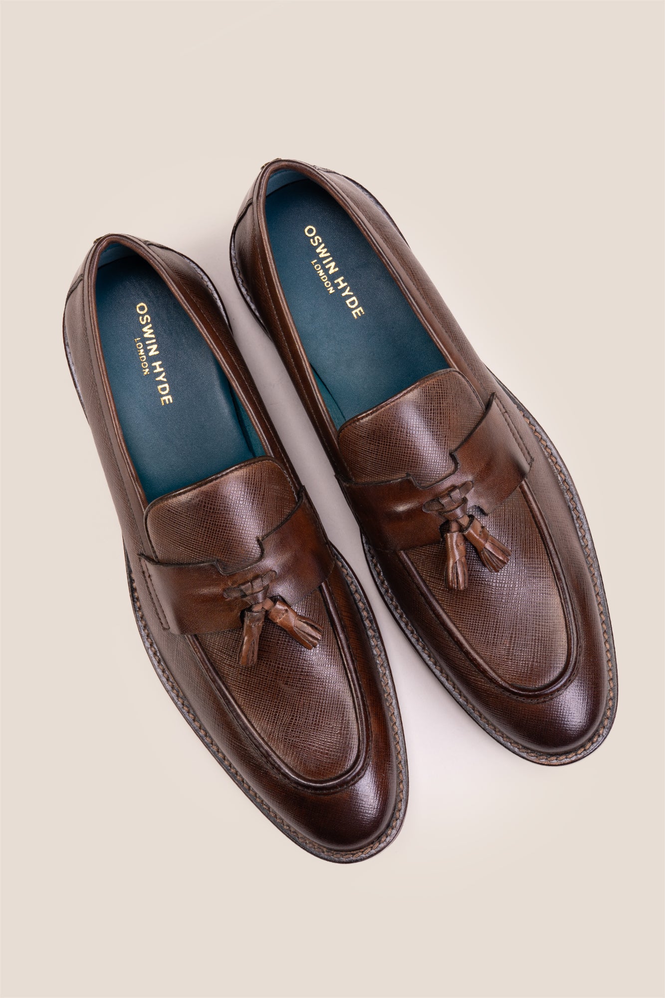 Premium brown leather tassel loafers for men featuring a textured finish, burnished moc-toe details, decorative leather tassels, and a cushioned teal interior.