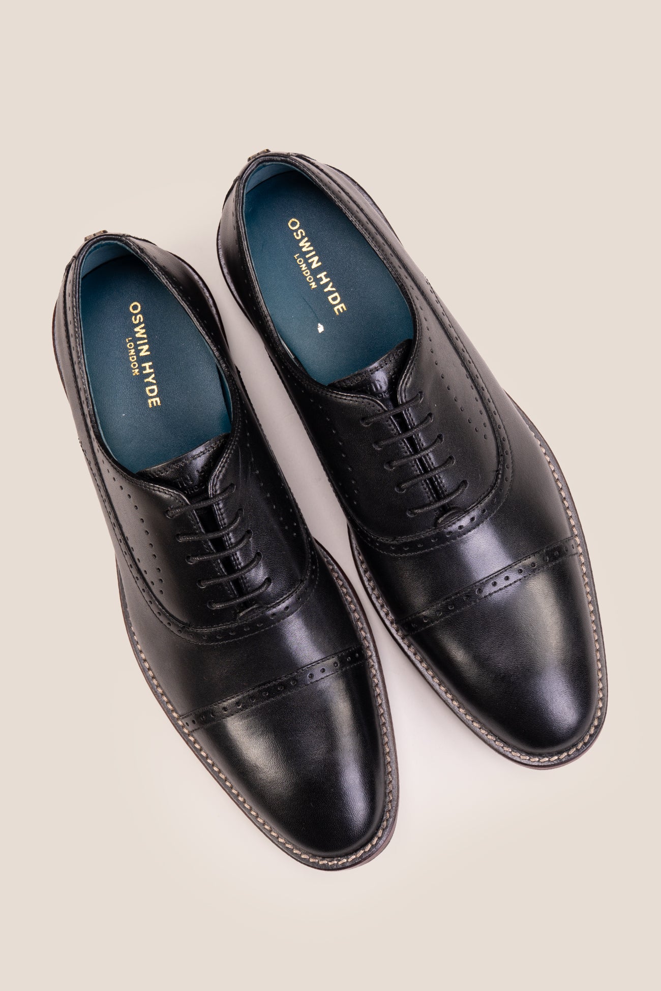 Premium men's black leather oxford shoes by Oswin Hyde London, featuring a cap toe with decorative perforations, closed lacing, contrast welt stitching, and a cushioned teal interior.